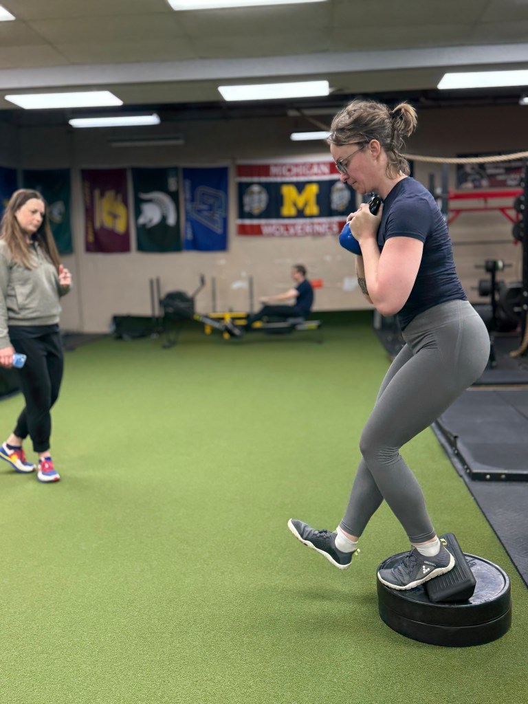 A woman exercises with a kettlebell while her personal trainer watches.